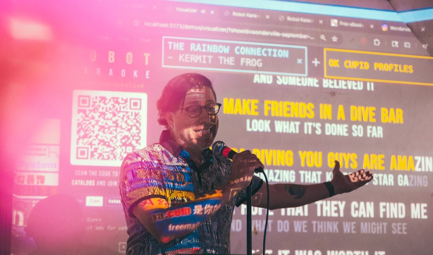 photo of a man in front of a screen being projected with lyrics and graphics speaking into a microphone